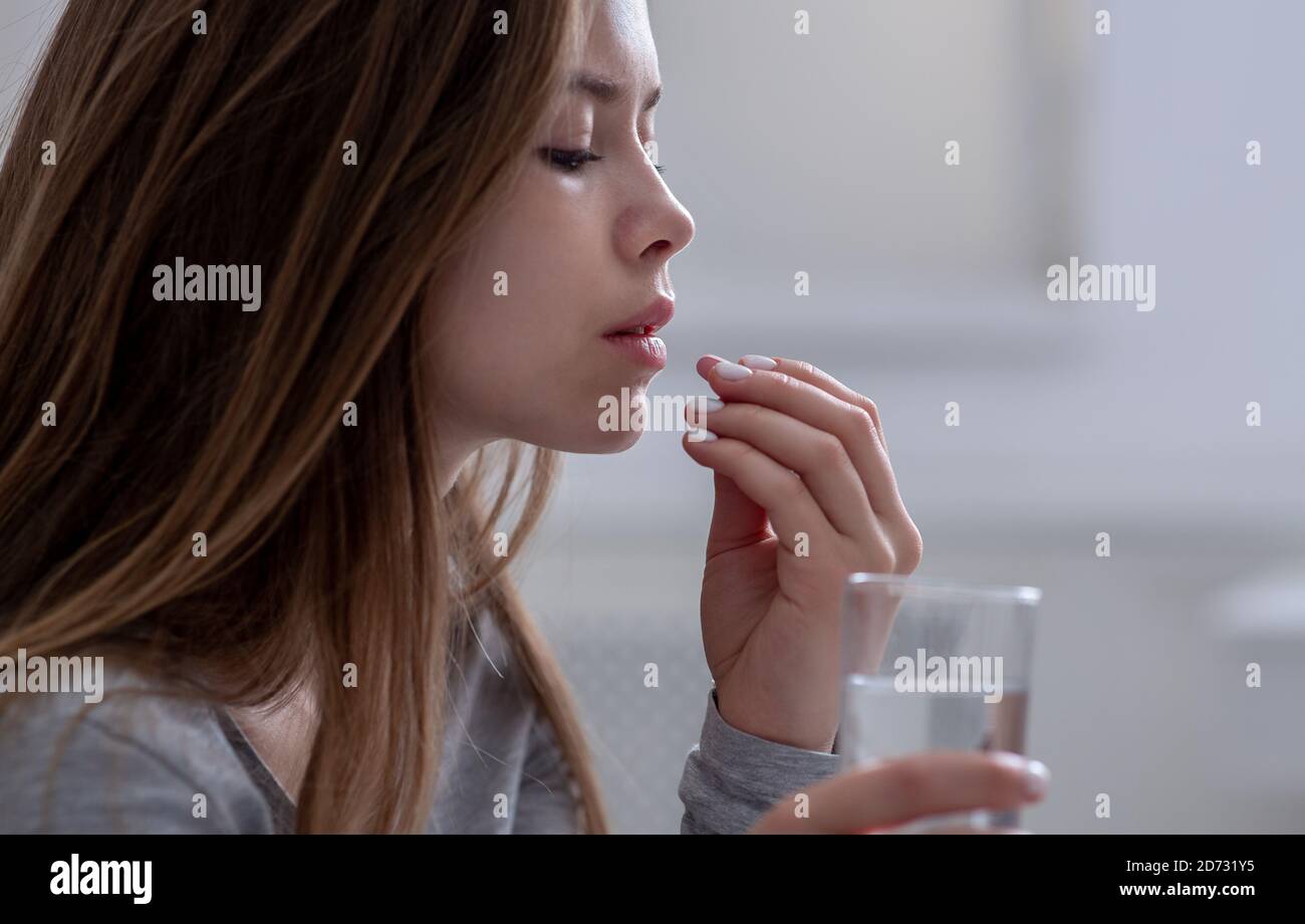Side view of young woman with glass of water taking sleeping pill or antidepressant, copy space Stock Photo