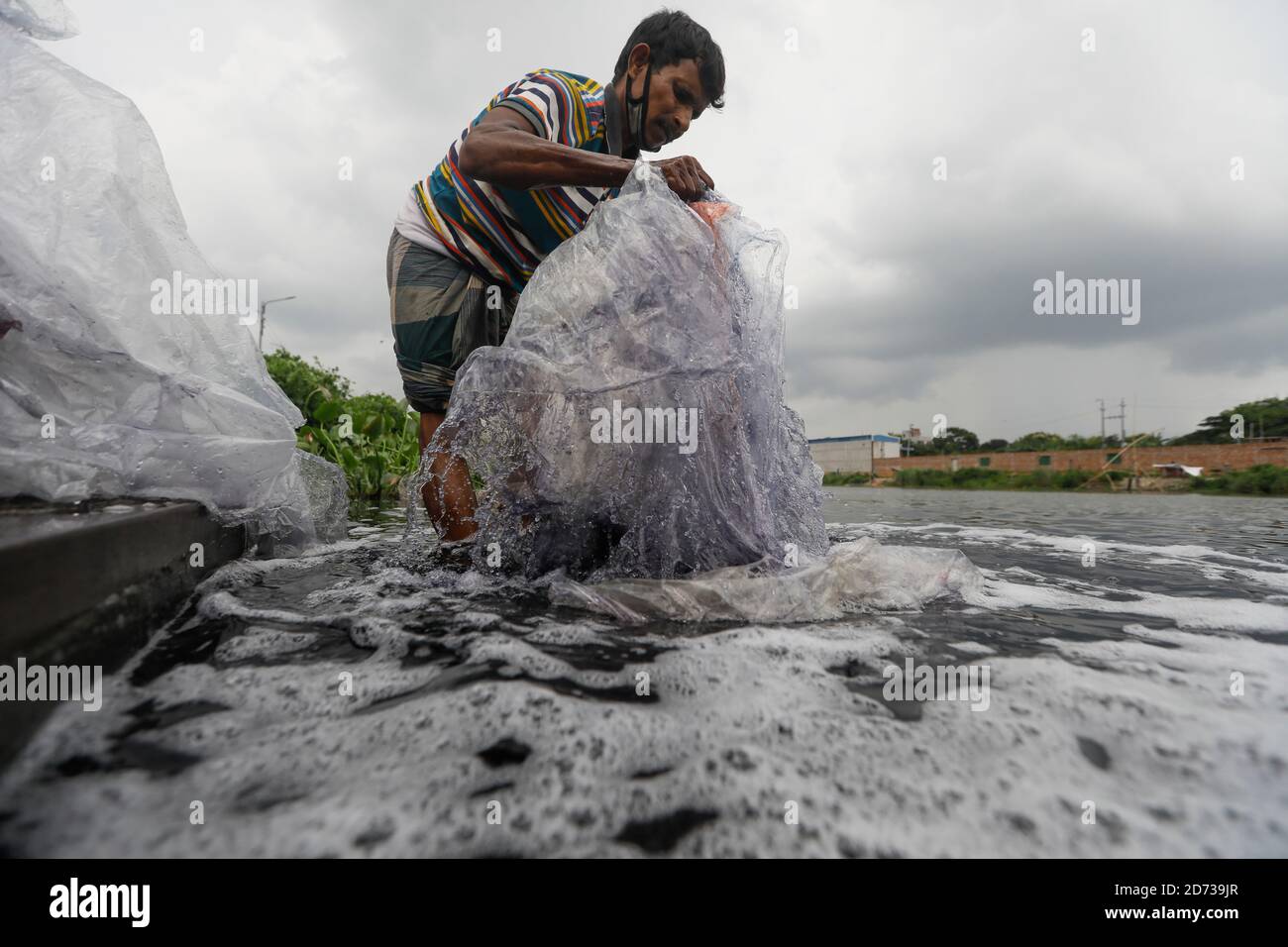A Bangladeshi man washes plastic waste, which were used to carry chemicals, in the water of the Turag River before recycling it, in Tongi, near Dhaka, Stock Photo