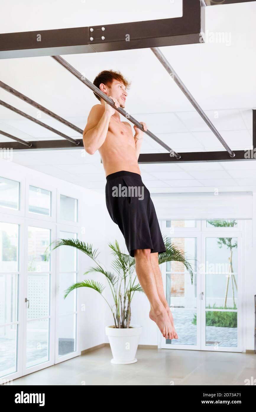 Man doing calisthenetic exercises pulling himself up on a bar with his arms to strengthen his muscles in a high key gym in a health and fitness concep Stock Photo