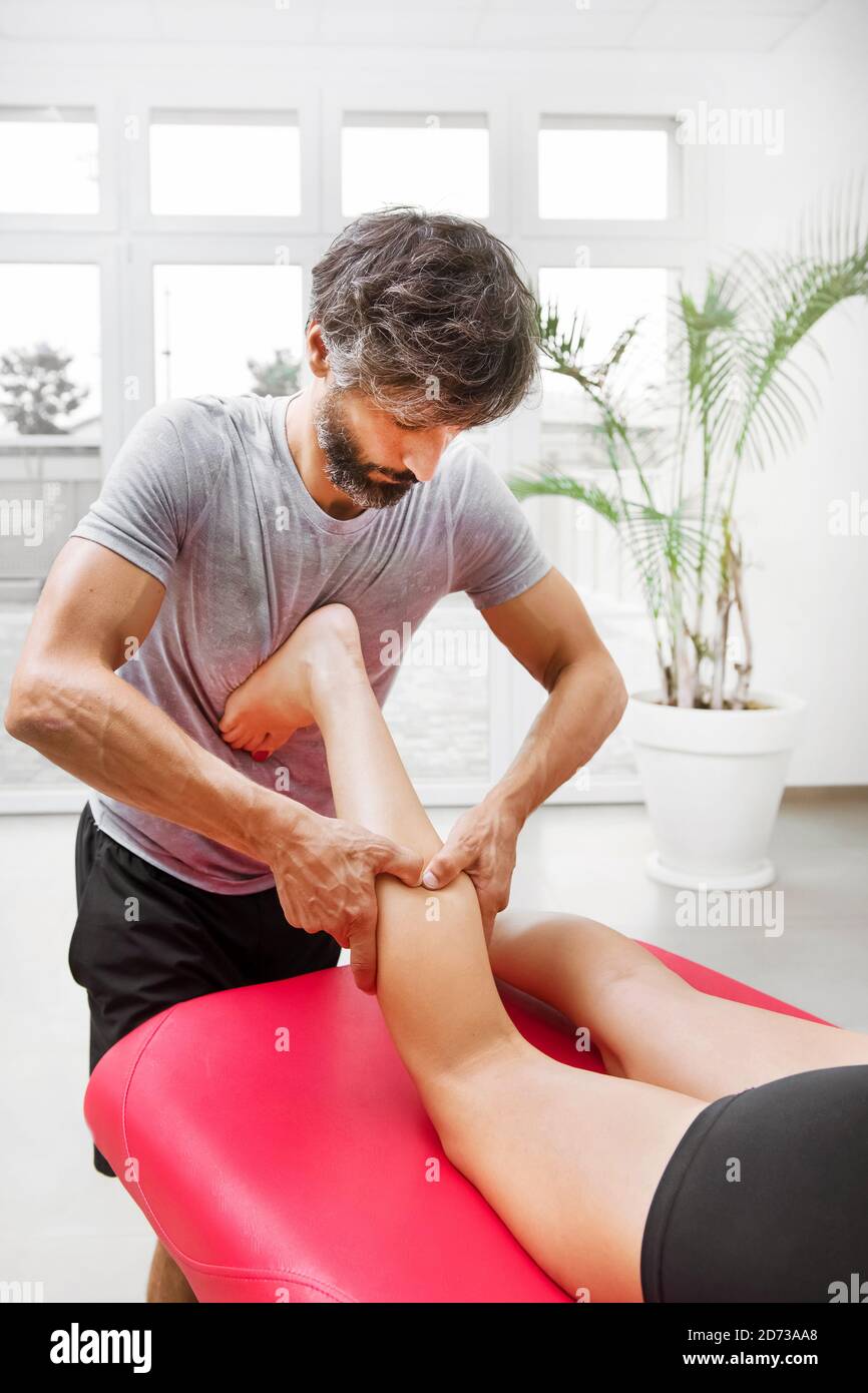 Male osteopath performing a calf myofascial massage on a young woman manipulating the muscles with his hands during a consultation in close up Stock Photo