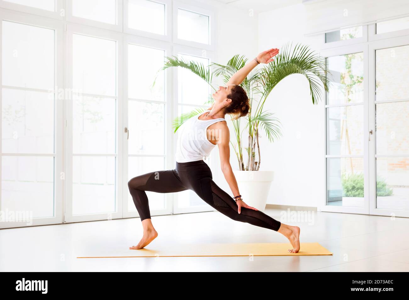 Young woman doing an Ashta Chandrasana yoga pose or high crescent lunge in a high key gym with copyspace in side view Stock Photo