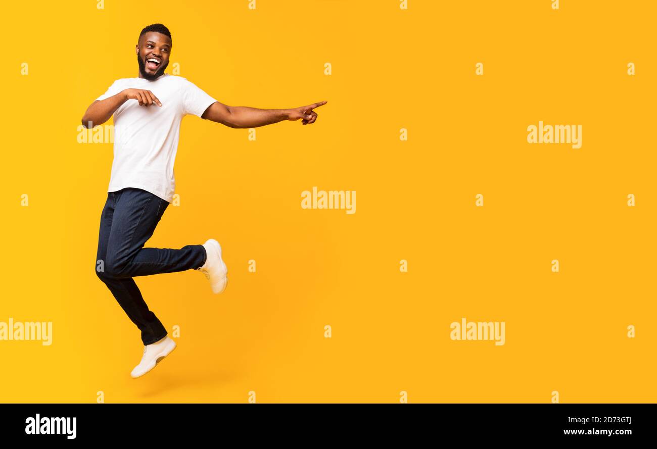 Joyful black guy jumping up and pointing aside Stock Photo - Alamy