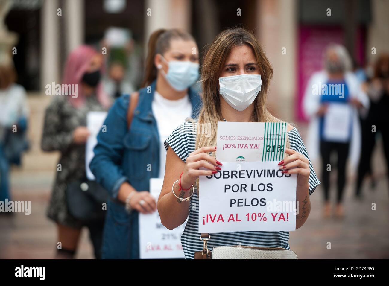 Protesters wearing face masks hold placards expressing their opinions at Plaza de la Constitucion square during the demonstration.The association of hairdresser and Malaga beauty association  demand the government to lower VAT rate from 21% to 10% for their sector, which is considered an 'essential jobs' under the context of the coronavirus pandemic. The hairdressers and beauty centres were closed due to the coronavirus pandemic and many of them have lost their incomes, after it reopening with restrictions and limit capacity. Stock Photo