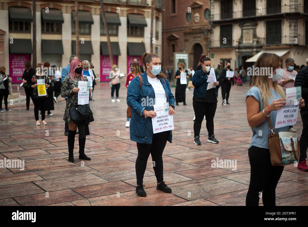 Protesters wearing face masks hold placards expressing their opinions at Plaza de la Constitucion square during the demonstration.The association of hairdresser and Malaga beauty association  demand the government to lower VAT rate from 21% to 10% for their sector, which is considered an 'essential jobs' under the context of the coronavirus pandemic. The hairdressers and beauty centres were closed due to the coronavirus pandemic and many of them have lost their incomes, after it reopening with restrictions and limit capacity. Stock Photo