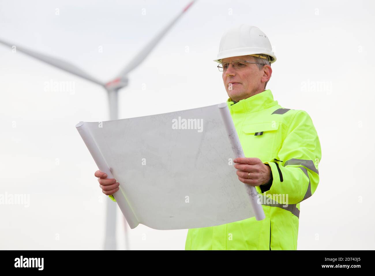 Mature engineer standing in front of a wind turbine with blueprint in his hand - focus on the face Stock Photo