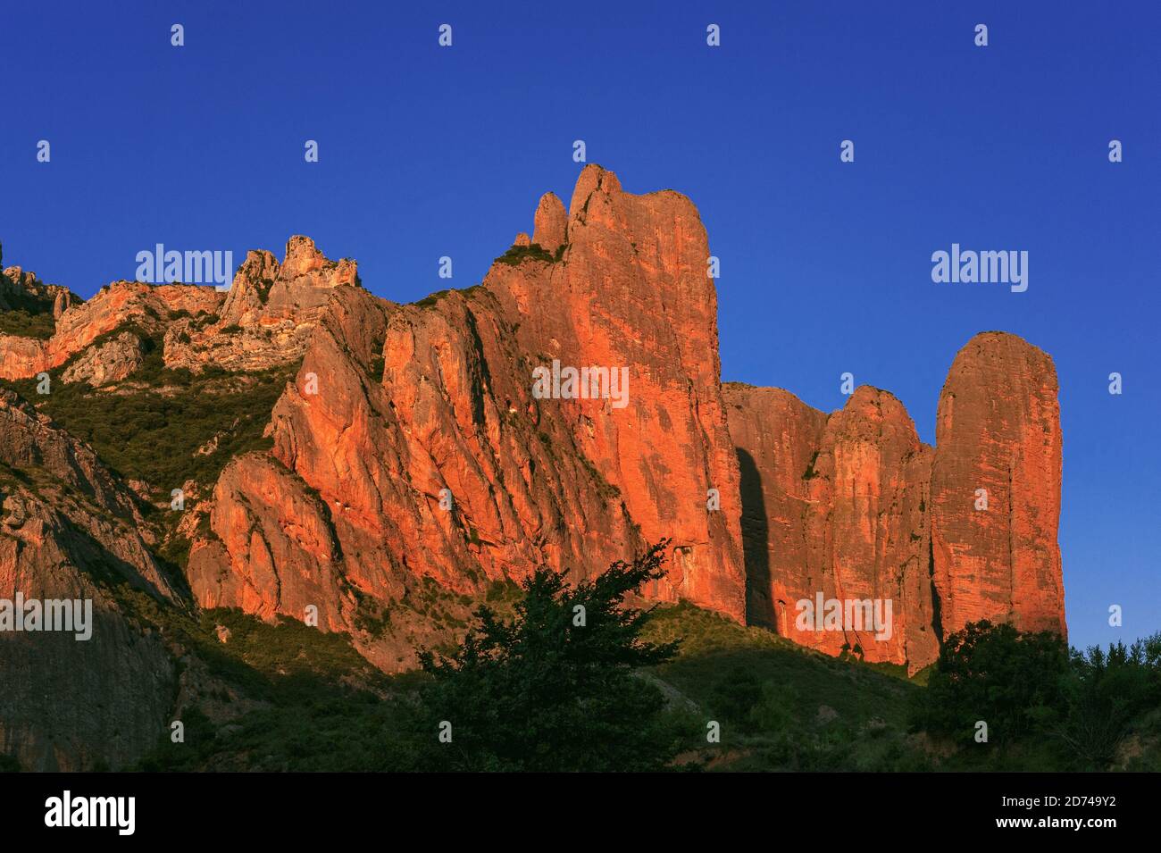 The majestic Mallos de Riglos, a spectacular natural gateway to the Pyrenees, glow bright orange-red in evening sunlight in Huesca Province, Aragon, Spain.  Los Mallos (The Mallets) formed at least 20 million years ago, when material washed down from Pyrenean slopes compacted with limestone to form conglomerate rock.  The distinctive ‘mallets’, sculpted by erosion, are a physical border between the Pyrenean foothills and the Ebro Basin, rising to around 300 m (980 ft).  In the 11th century, the Mallos area was briefly an independent kingdom after Pedro, King of Aragon, gave it as a dowry. Stock Photo