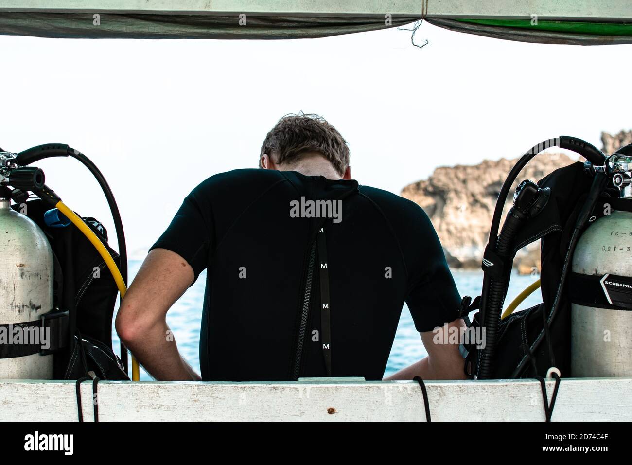 A scuba diver in a wetsuit between two oxygen tanks preparing for his