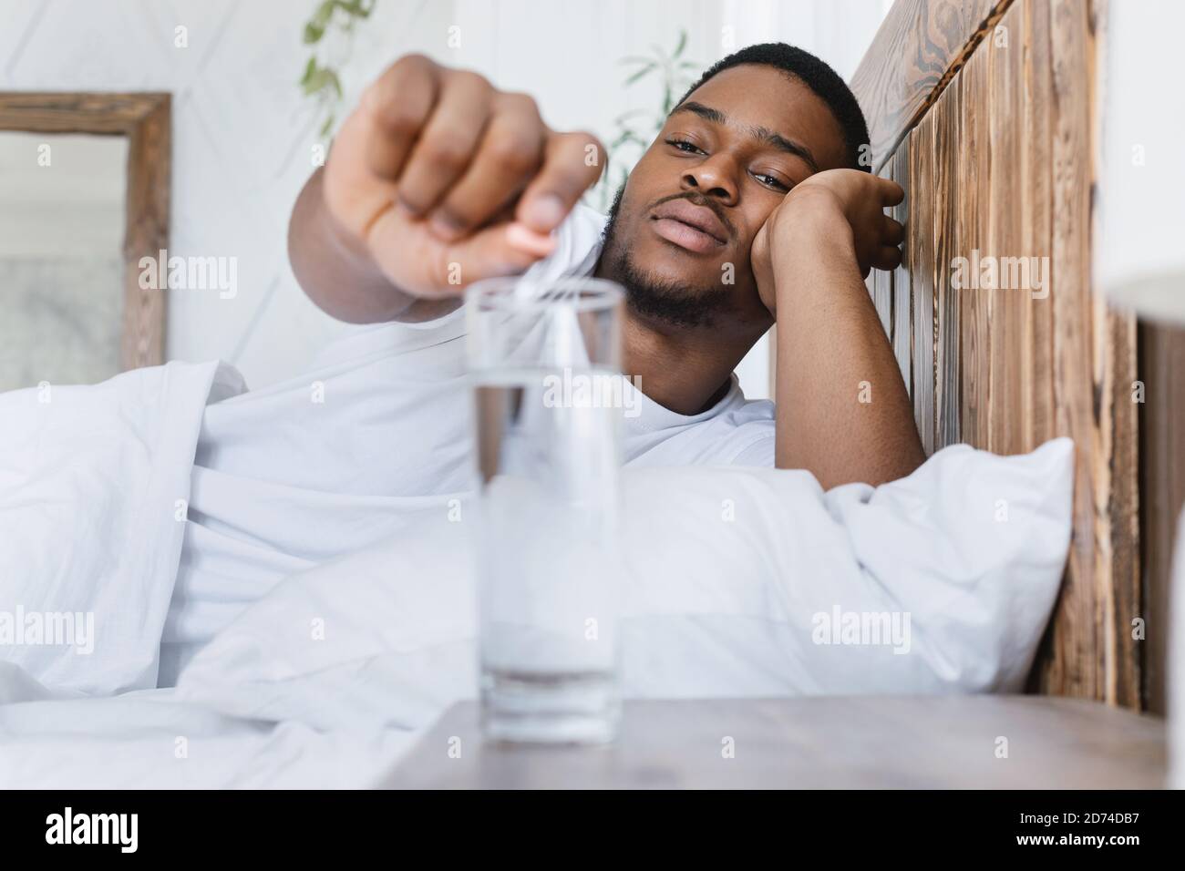 Sick African Guy Putting Pill Into Glass Lying In Bed Stock Photo