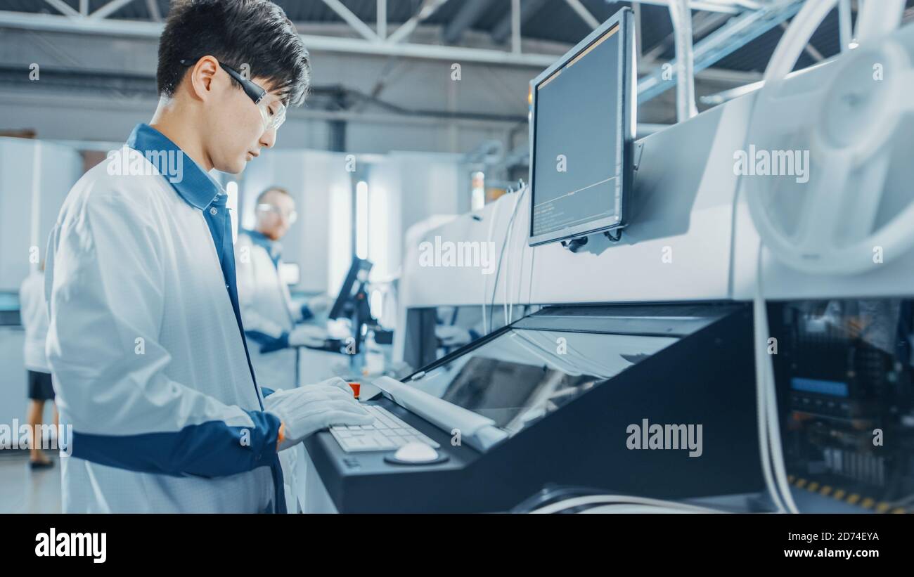 On High Tech Factory Asian Engineer Uses Computer for Programming Pick and Place Electronic Machinery for Printed Circuit Board Assembly Line Stock Photo