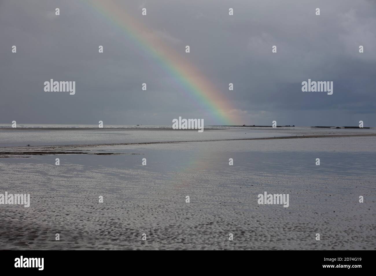 Rainbow in-between dark clouds over the Golden Beach in the Normandie, France. Stock Photo