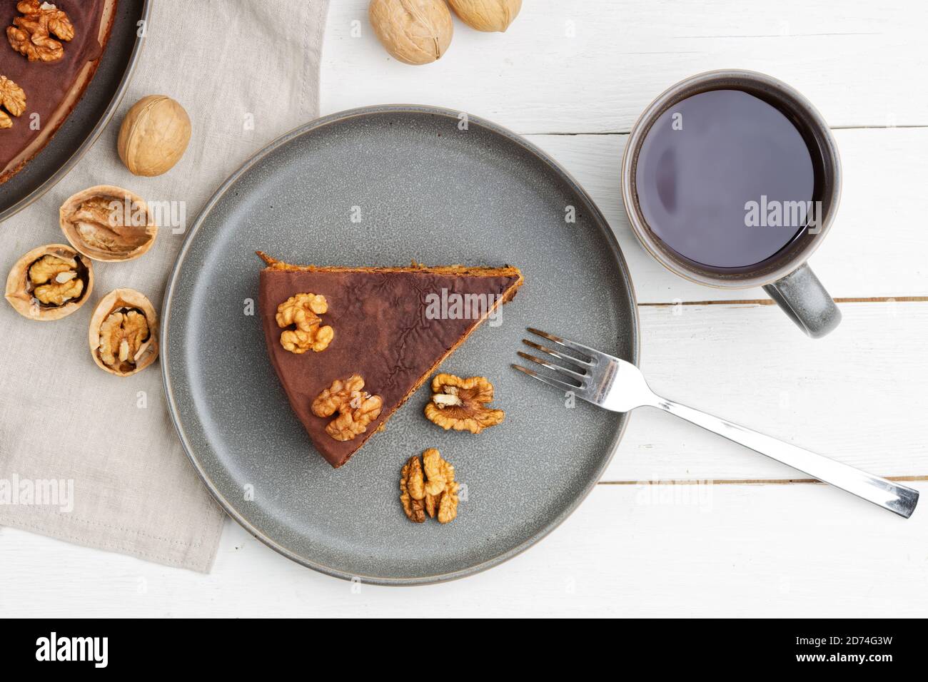 Homemade Walnut Cake with Chocolate Icing and mug of hot tea on white wooden table. Top view. Stock Photo