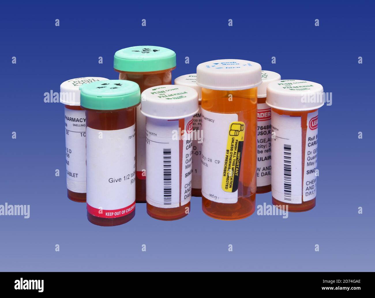 A variety of orange tinted plastic prescription pill bottles with safety lids and labels isolated on a blue background. Stock Photo