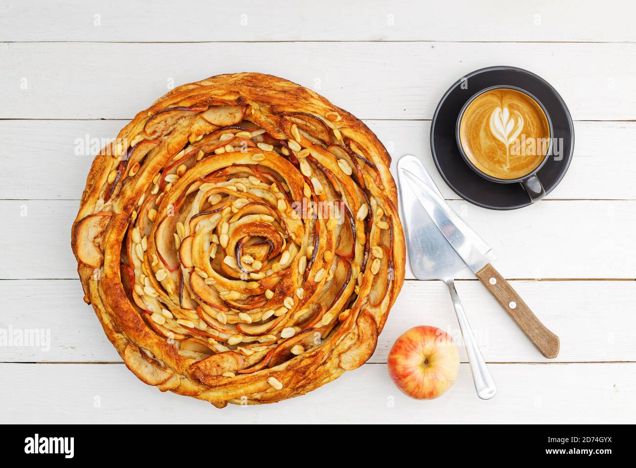 Fresh baked homemade apple and cinnamon puff pastry swirl pie and cup of coffee on white wooden table. Top view. Stock Photo