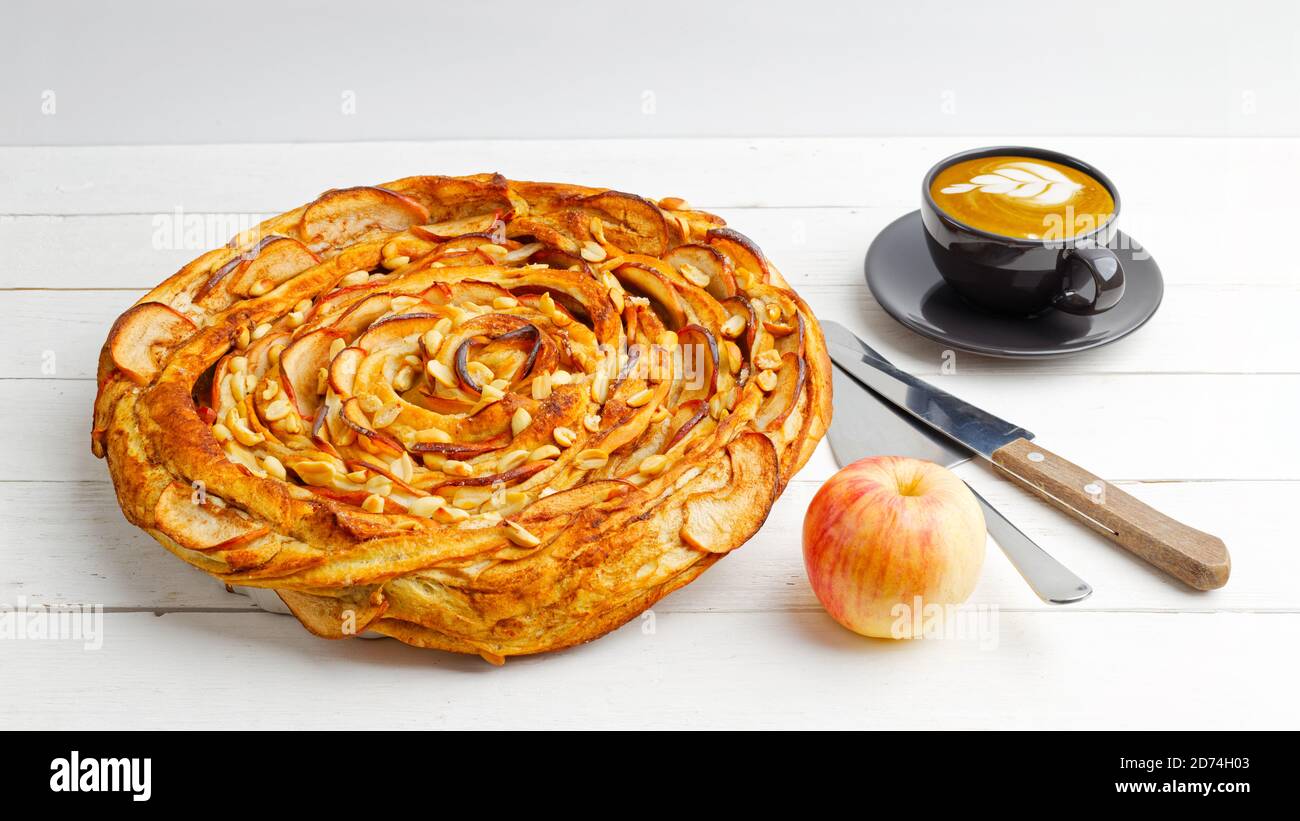 Fresh baked homemade apple and cinnamon puff pastry swirl pie and cup of coffee on white wooden table Stock Photo