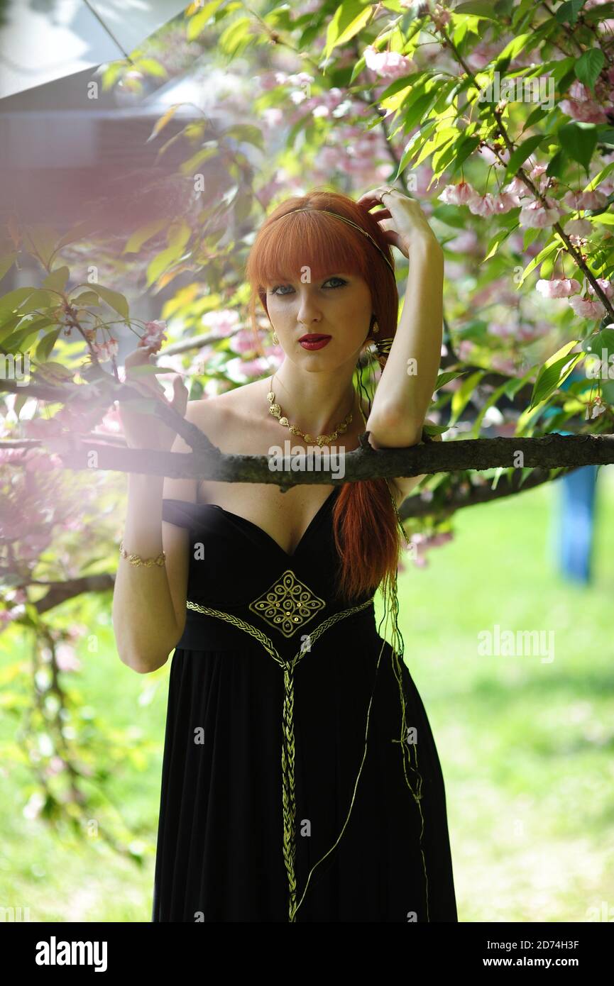 Young beautiful woman with red hair in a black long dress in a spring ...