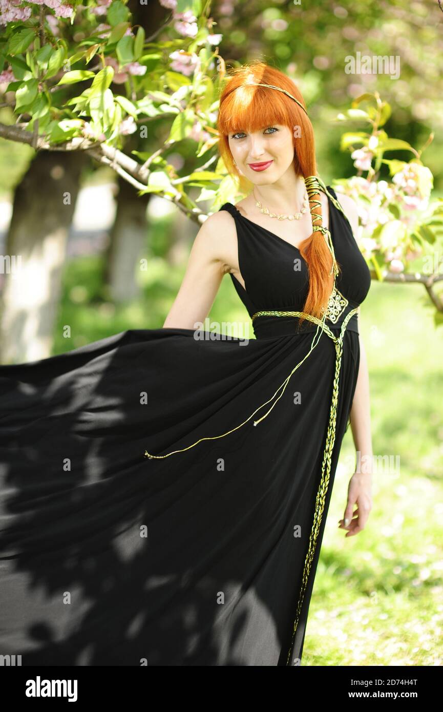 Young beautiful woman with red hair in a black long dress in a spring ...