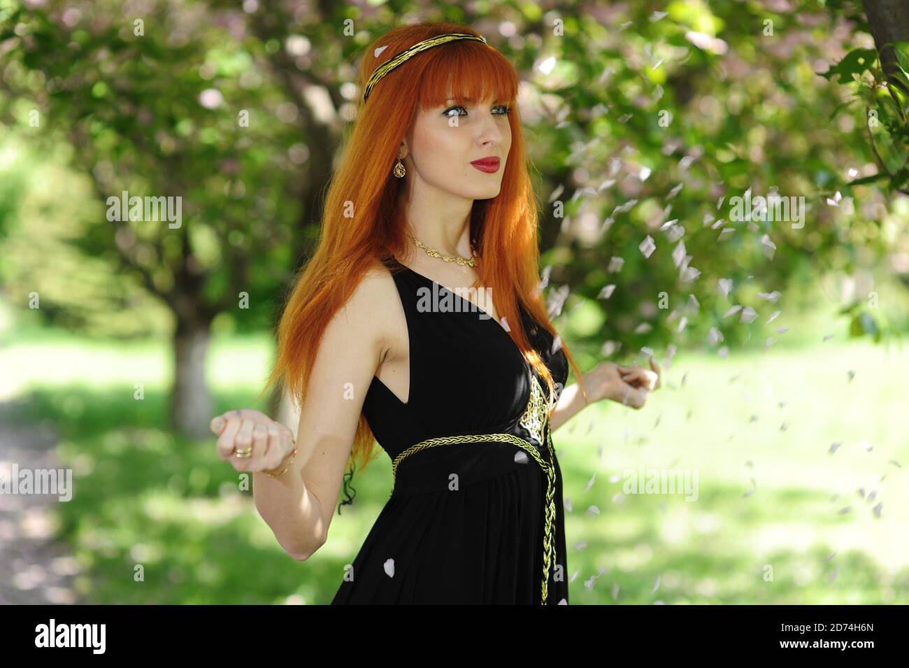 Young beautiful woman with red hair in a black long dress in a spring ...