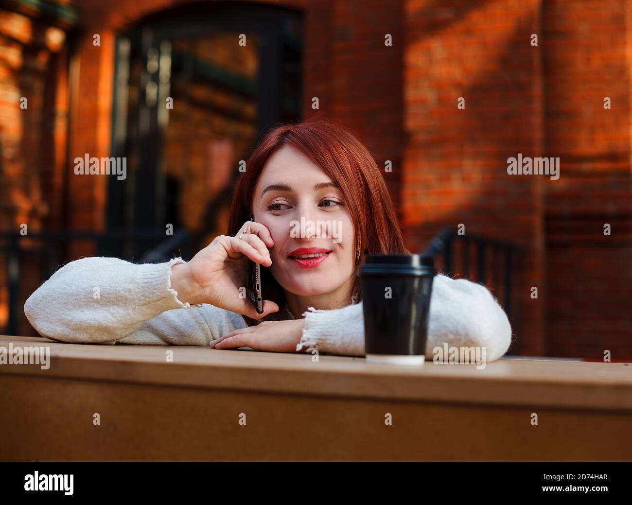 Smiling woman leaned on bar table talking on mobile. Female chatting with friend on a phone. Stock Photo