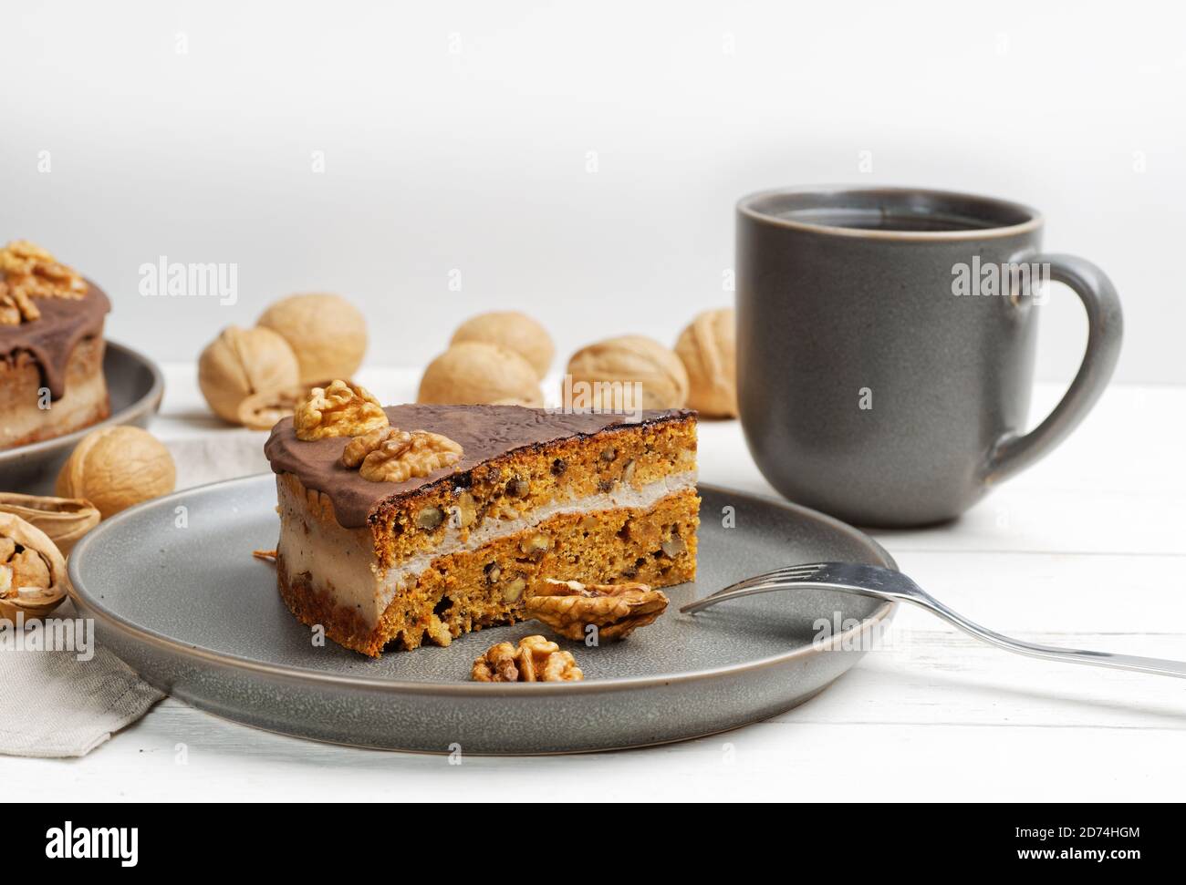 Piece of homemade walnut cake with chocolate icing and mug of tea on white wooden table. Shallow focus. Stock Photo
