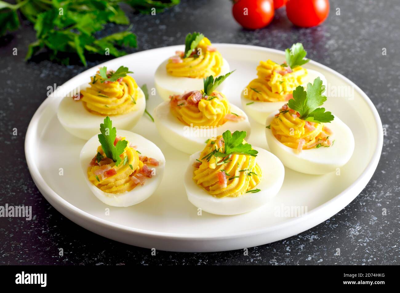 Deviled stuffed eggs with egg yolk, bacon, mustard and parsley on dark stone background, close up view Stock Photo