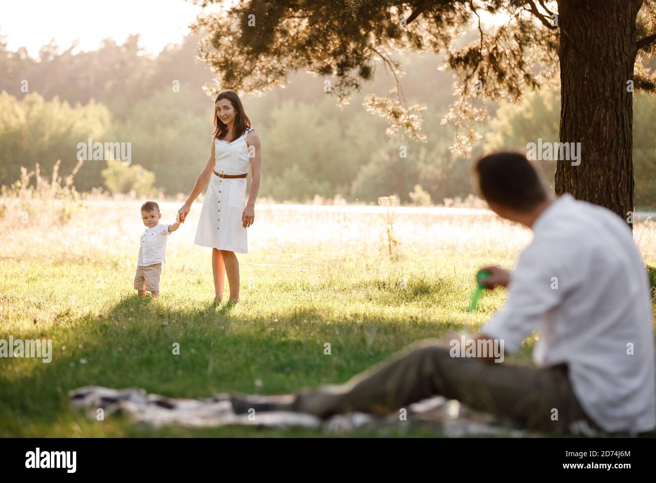 father, mother and son blow soap bubbles in the park together on a sunny summer day. happy