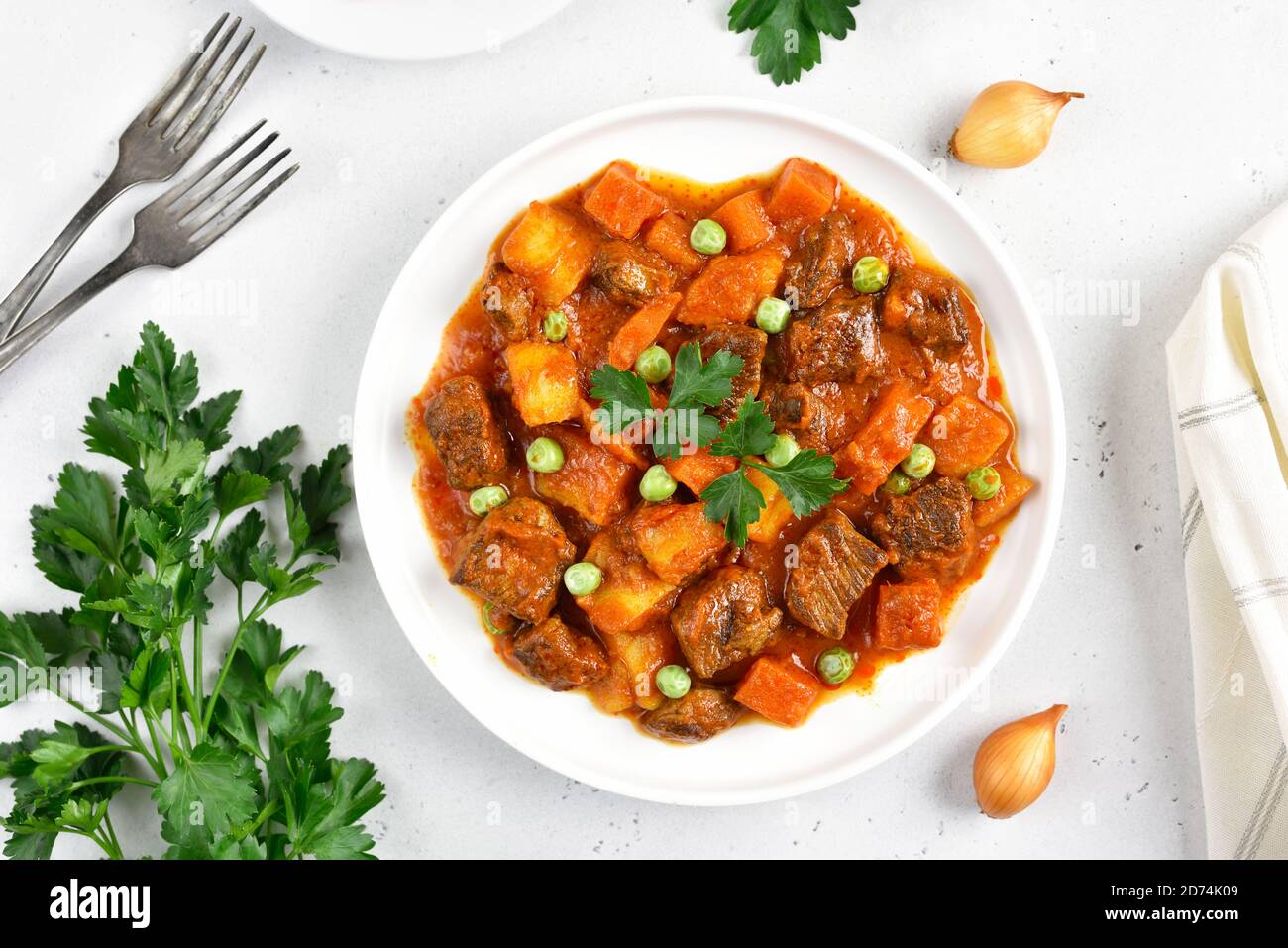 Homemade beef stew with potatoes and carrots in tomato sauce on  white plate. Top view, flat lay Stock Photo
