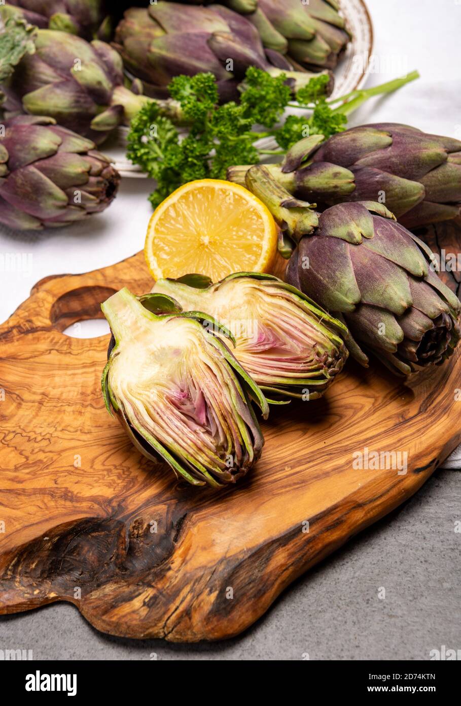 Fresh french petit violet artichokes heads cultivted in Brittany, France with lemon and parsley close up Stock Photo