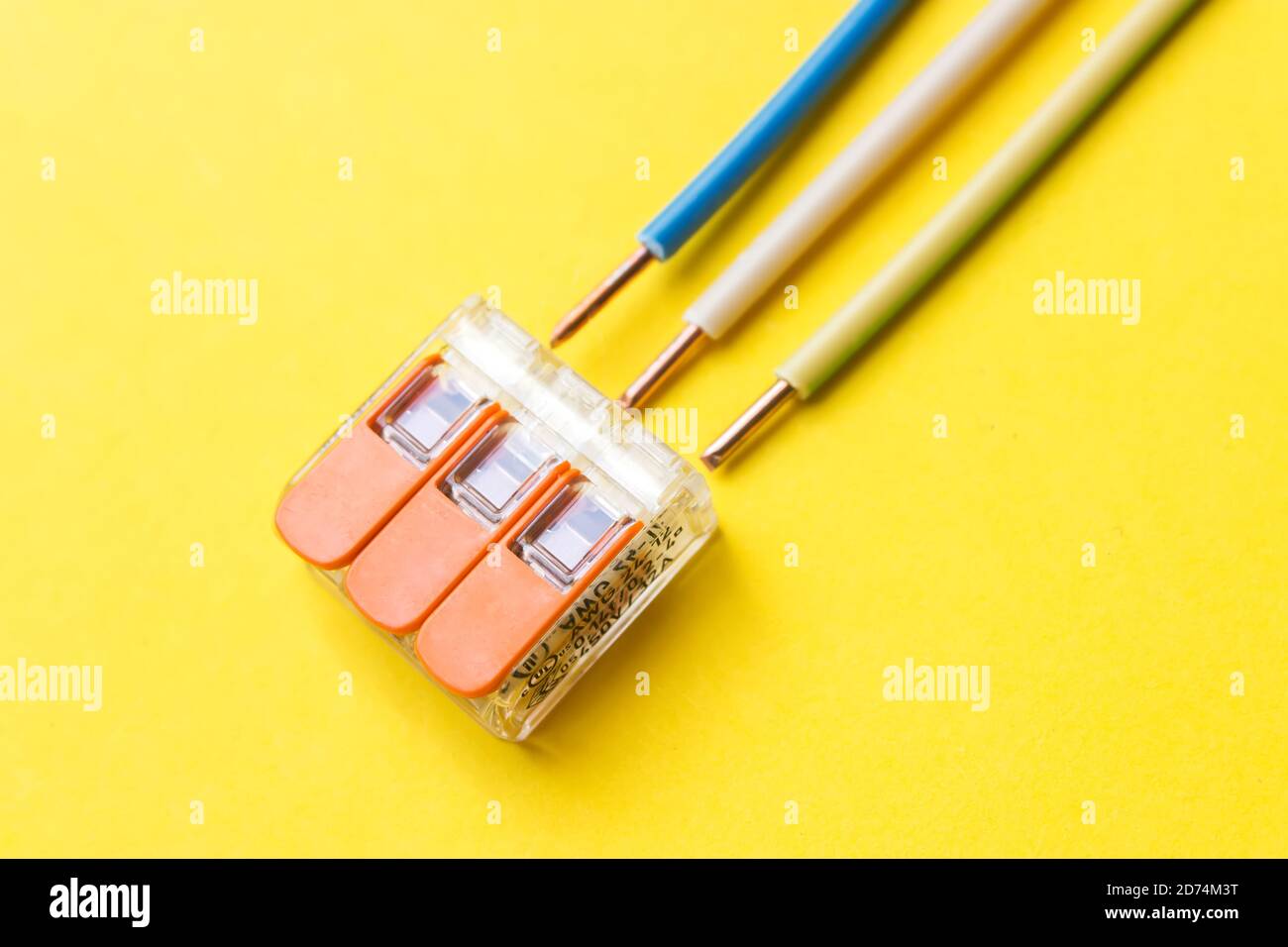 Compact splicing connector with wires phase, zero, ground on yellow background. Electronic components. Used for connecting wires without the need for Stock Photo