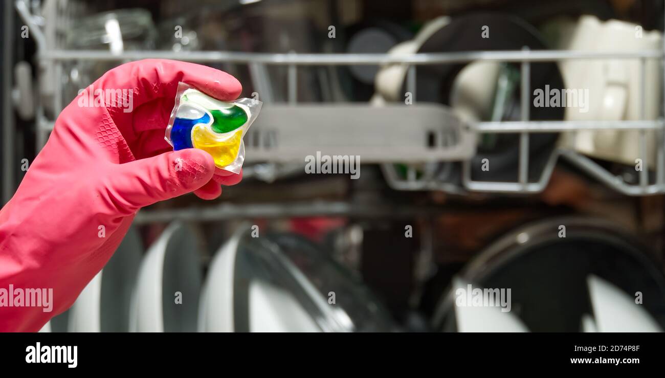 Dishwasher Detergents in hands. hands in pink golvs holds dishwasher