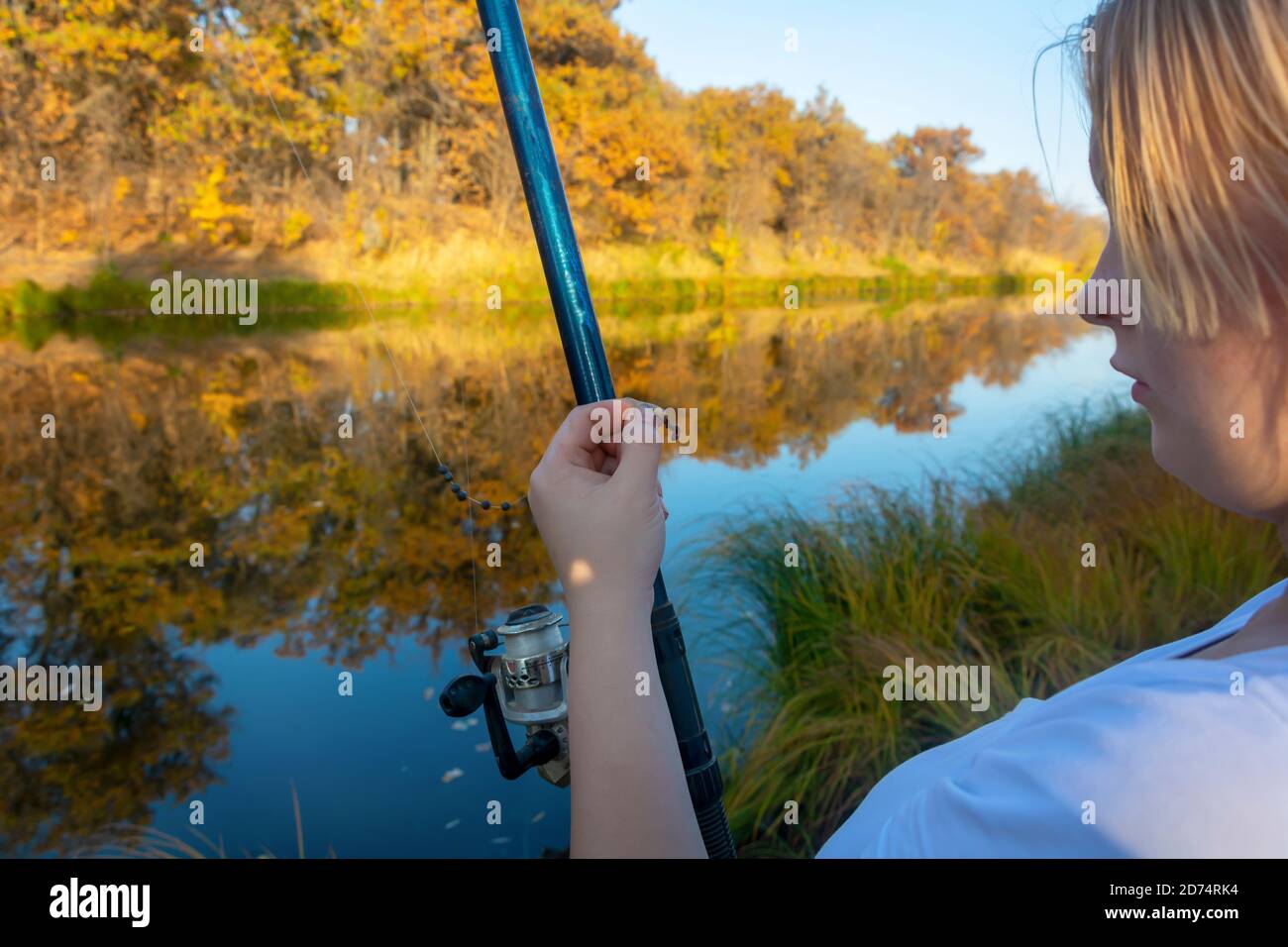 Young woman fisherman with fishing rod holds a hook with bait for fishing. Stock Photo