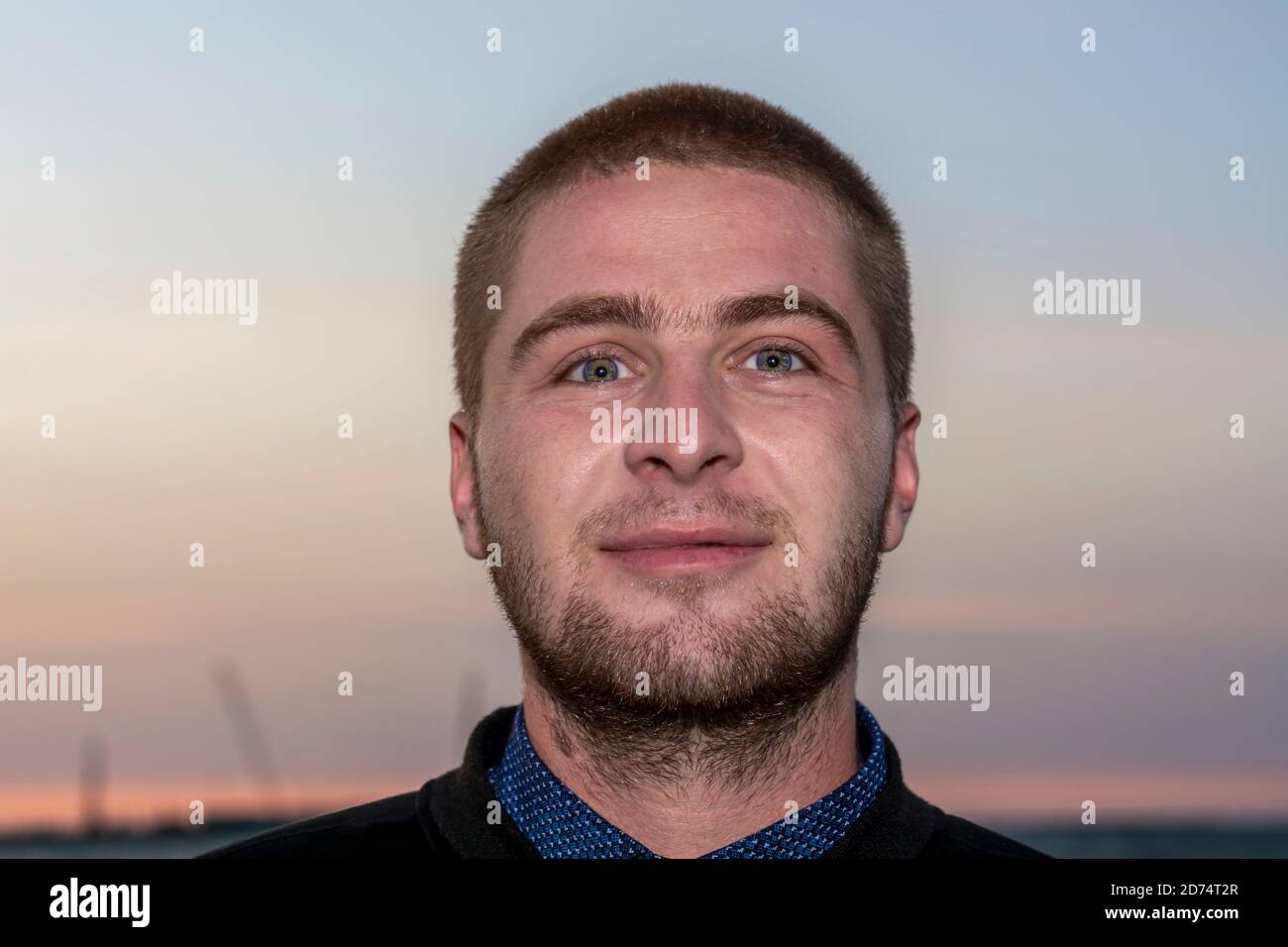 Close-up face of young Caucasian man against the sky at sunset. Smile on her face, an emotion of pleasure and happiness. Stock Photo