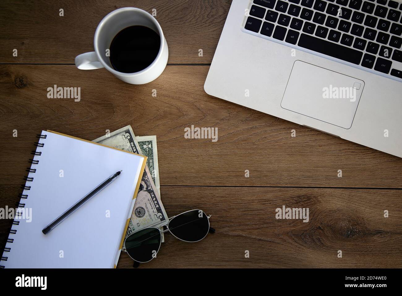 Top view of wooden desk with objects. Laptop, notebook, coffee cup, money, pen and sunglasses. Copy space. Stock Photo