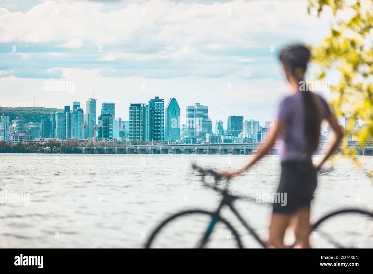 Montreal biking woman cyclist with bike looking at skyline view of condo towers and buildings downtown against Mount Royal landscape. Summer outdoor Stock Photo