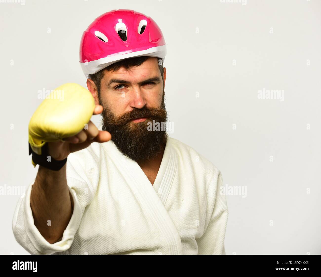 Man with beard in white kimono and pink helmet on white background. Karate man with flirty face