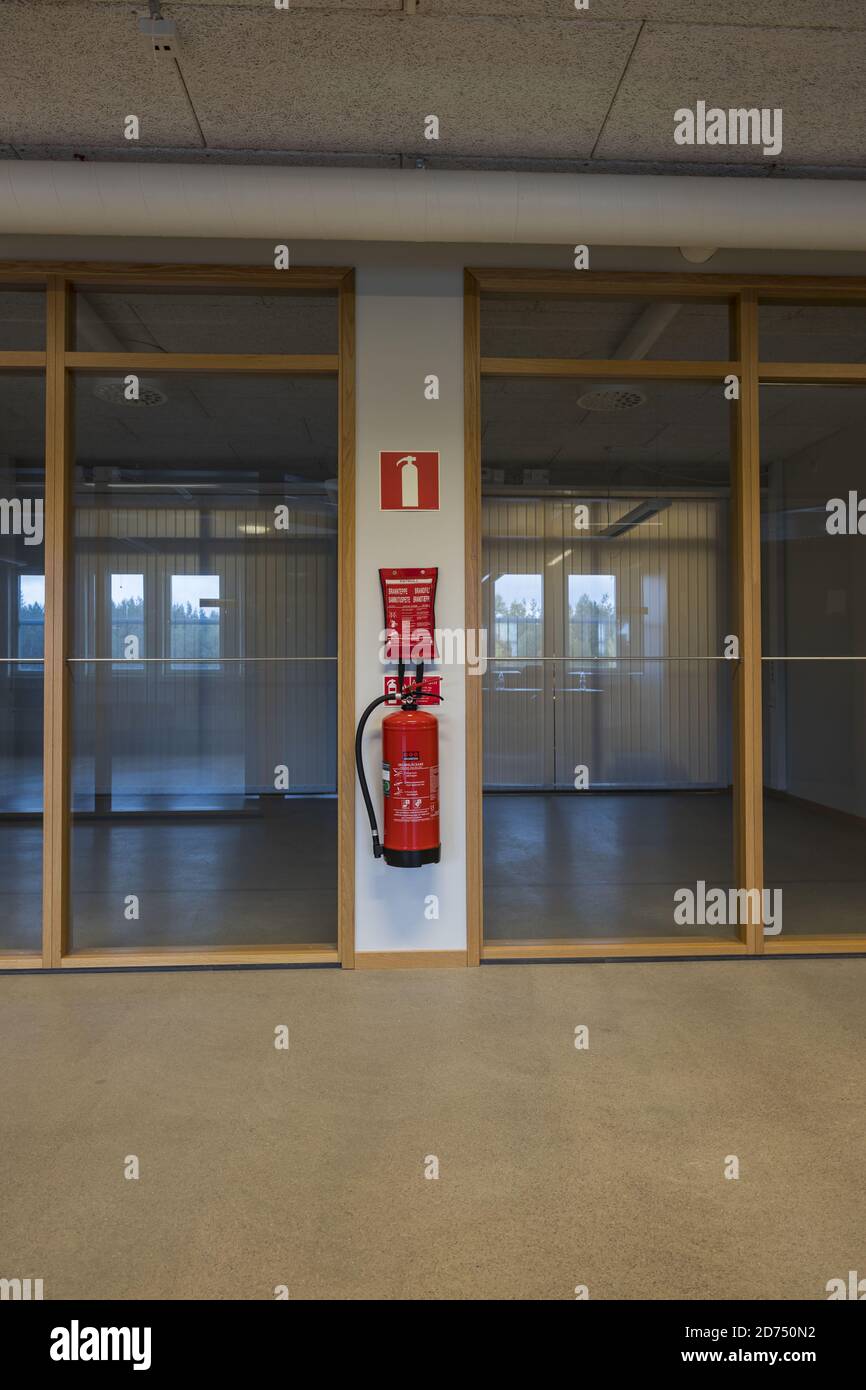 View of two empty office rooms with glass walls. Red fire extinguisher on white wall between offices. Stock Photo