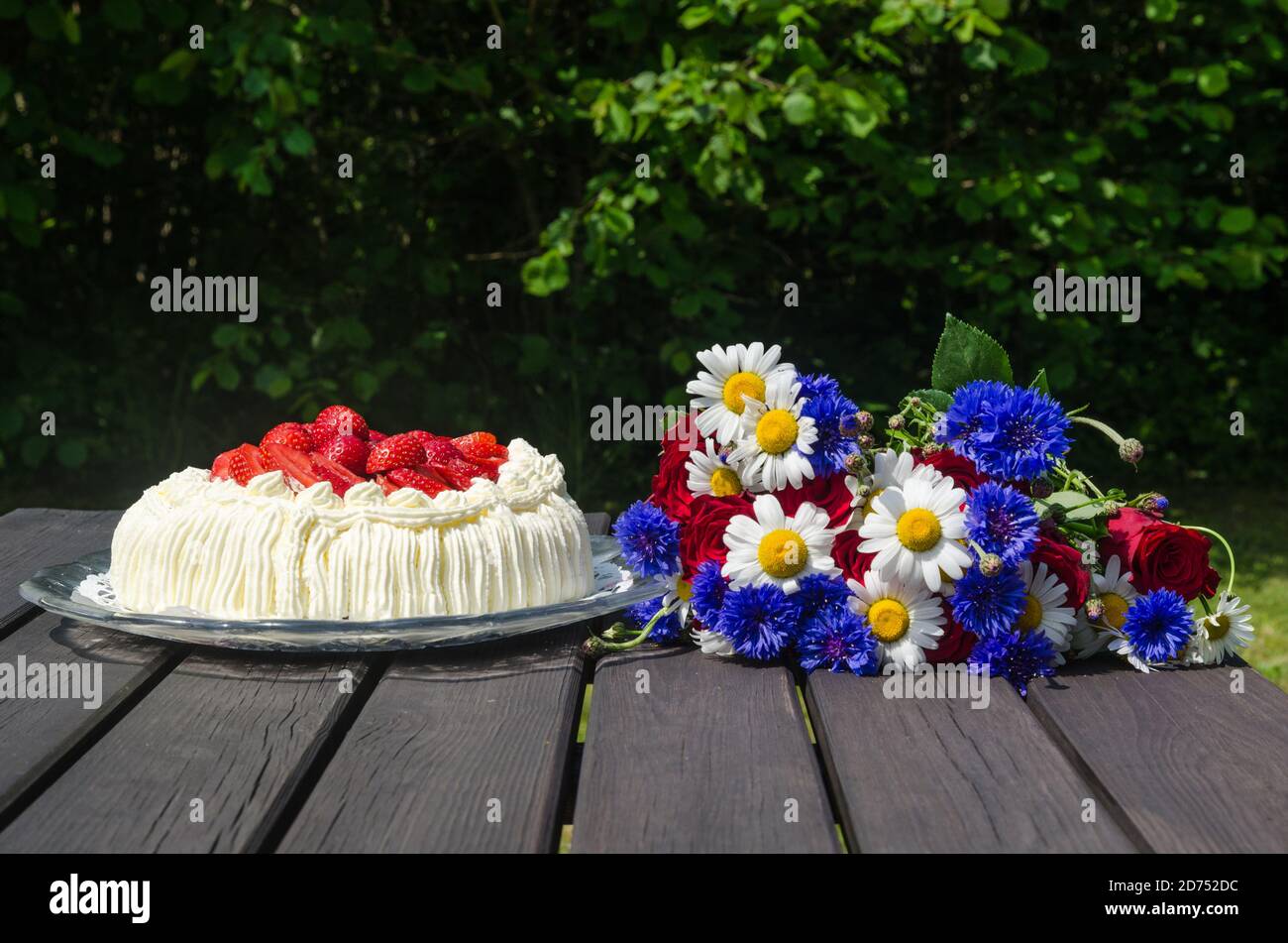 Atrawberry cream cake and summer flowers on a table in a garden Stock Photo