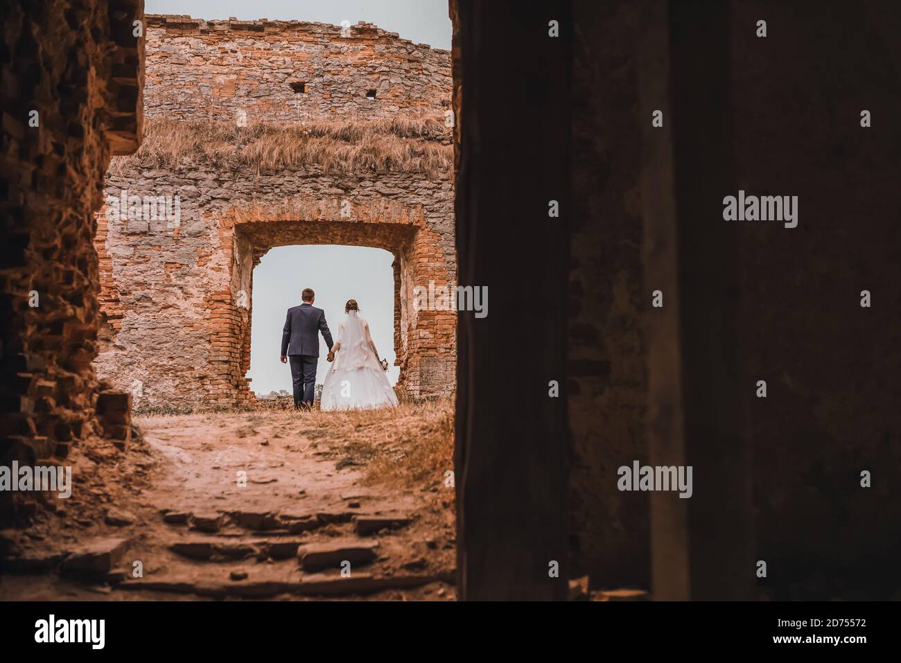 bride and groom are holding hands against the backdrop of brick ruins Stock Photo