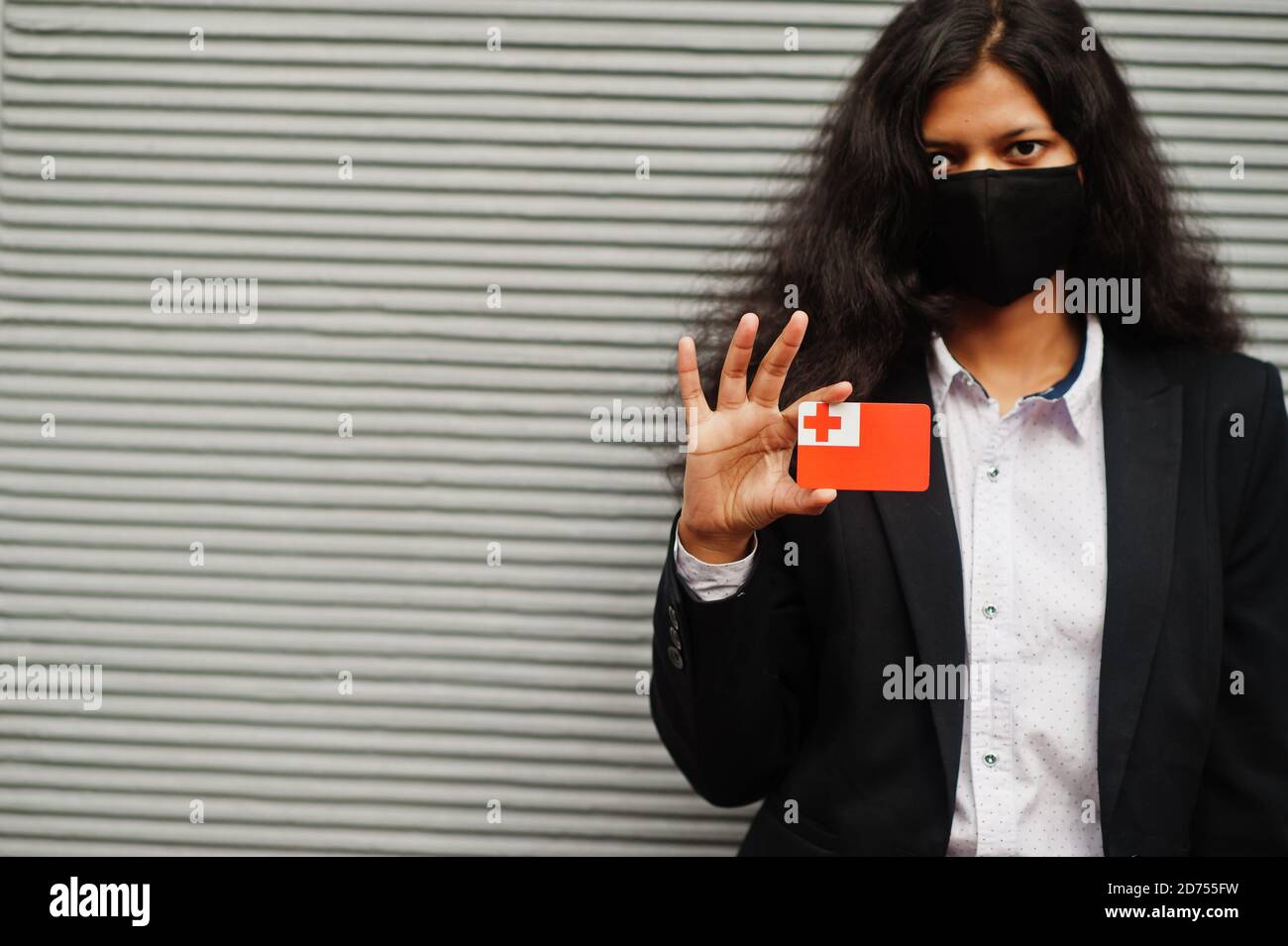 Asian woman at formal wear and black protect face mask hold Tonga flag at hand against gray background. Coronavirus at country concept. Stock Photo