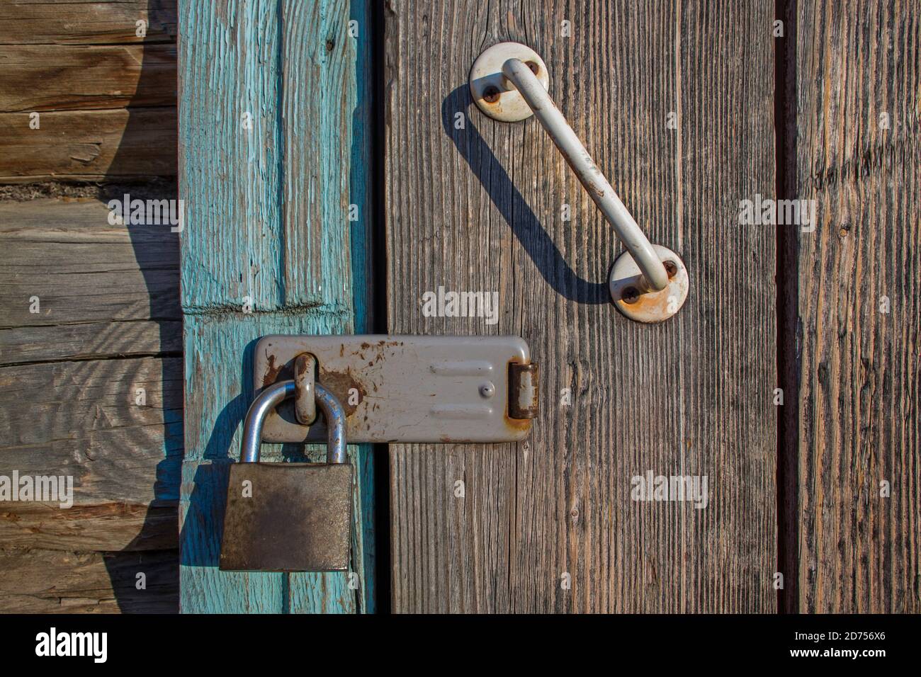 Old metal rusty lock on wooden door with white-painted, battered handle bolted on screws locked through bracket to door frame on bolt of log structure Stock Photo