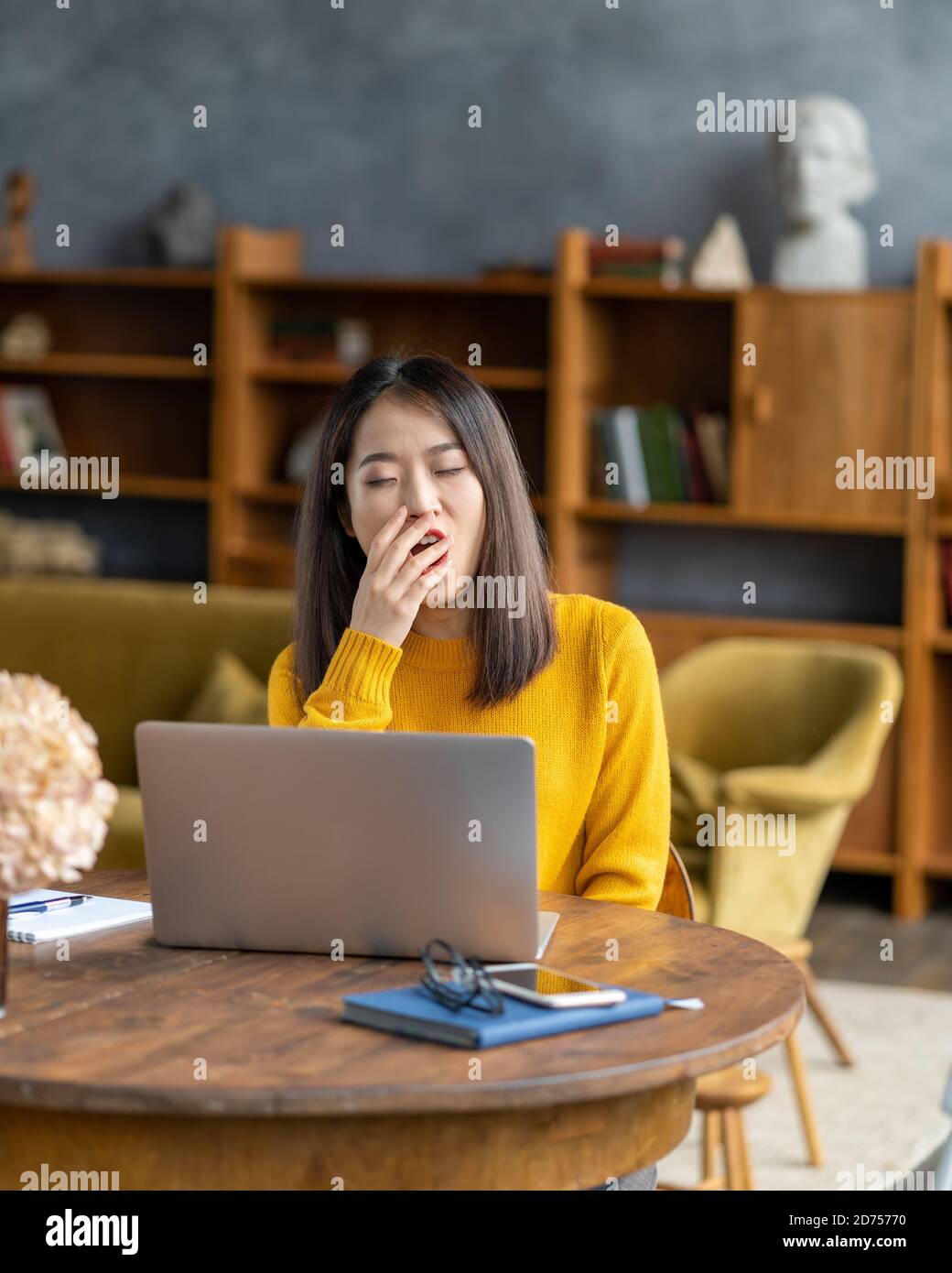 Asian woman yawning due to overworking and exhausting. Young lady in bright yellow jumper Stock Photo