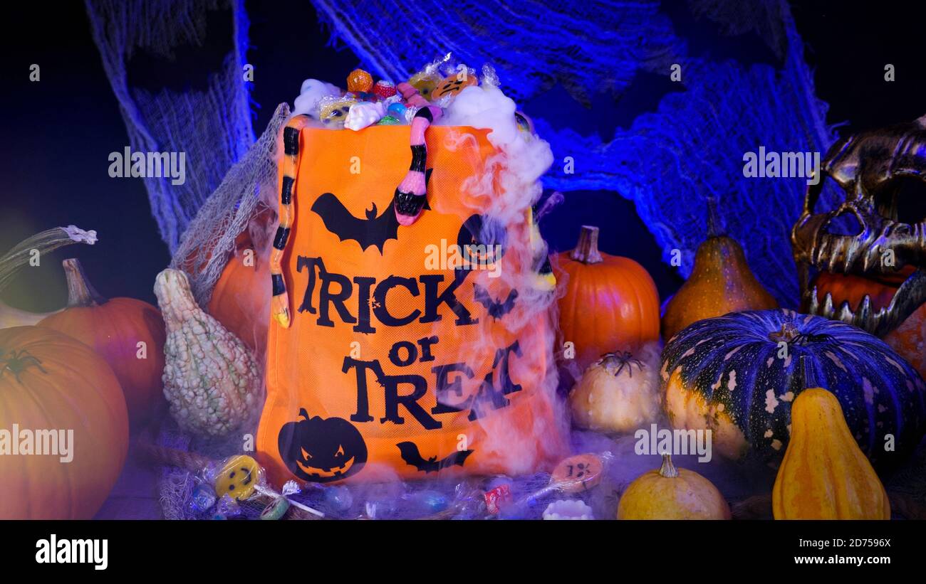 Halloween bag full of candies and sweets. Trick or treat, Halloween spooky scenery with pumpkins, misty fog, candies, skull, spiders and bats. Stock Photo
