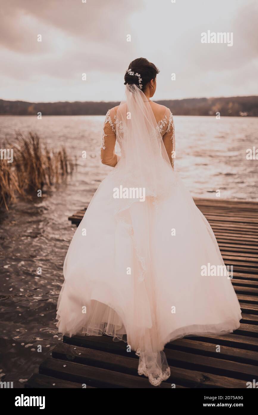 A young woman bride stands on a wooden brown pier Stock Photo