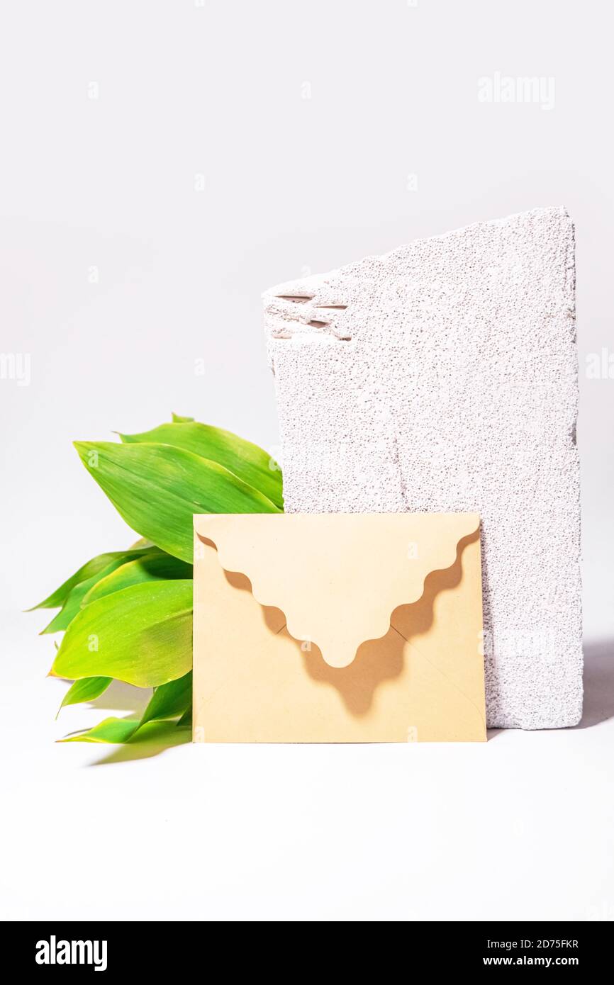 Natural background with craft envelope, green leaves and white textured stone. Still life wallpaper. Space for text. Mock up Stock Photo