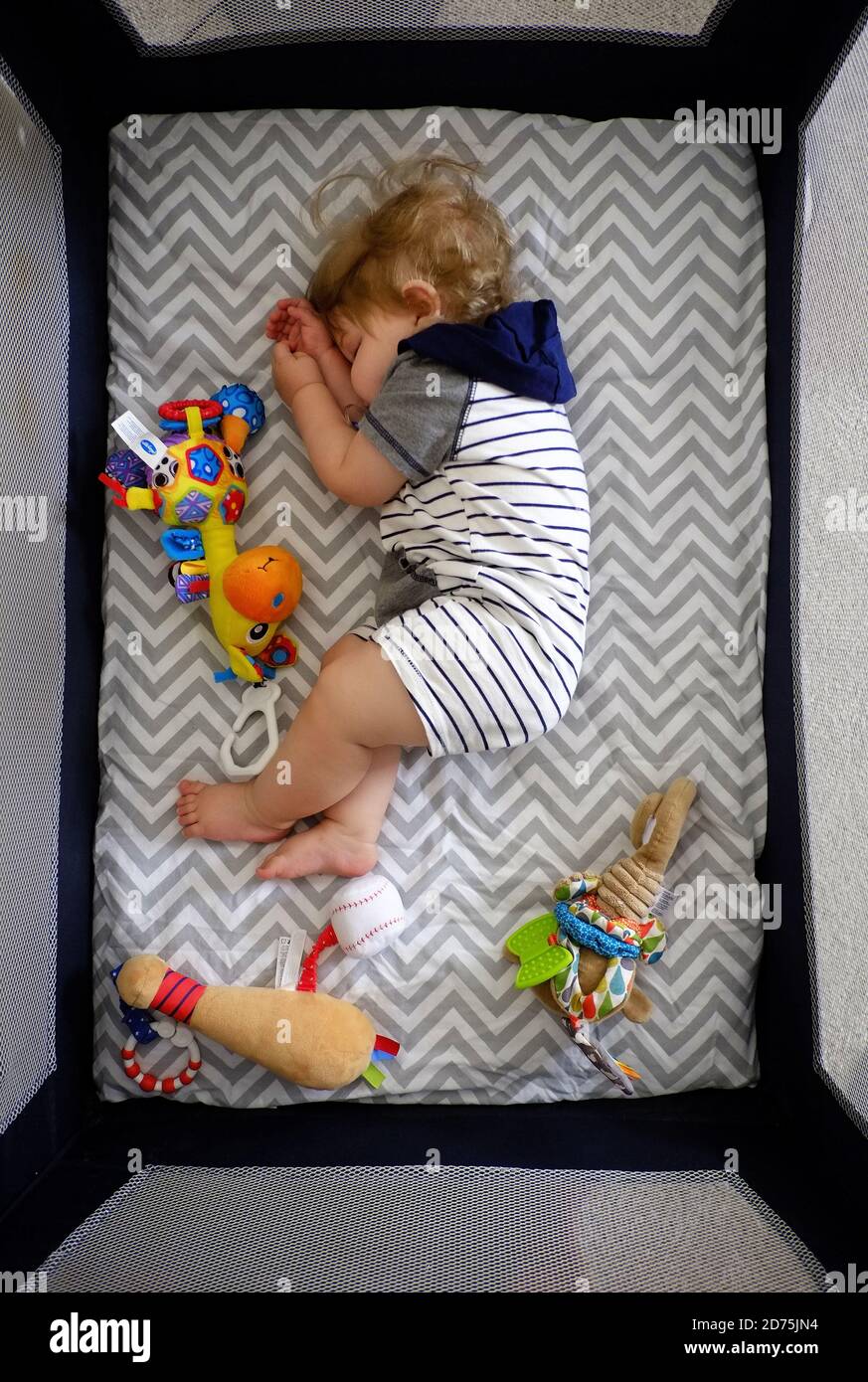 A one-year-old baby boy sleeping in a crib with toys. Stock Photo