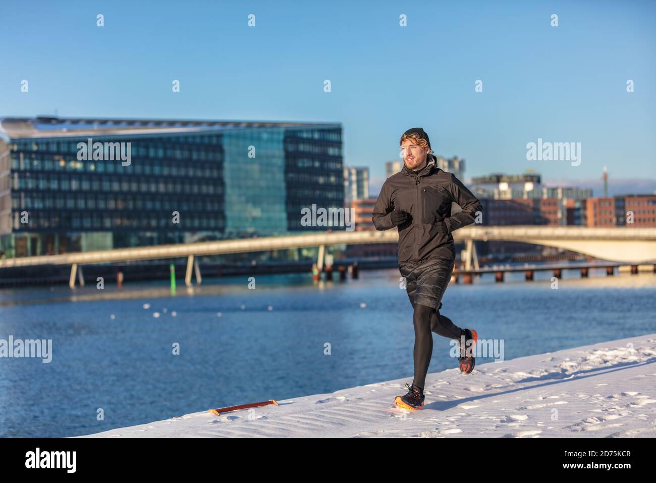 Winter running man wearing cold weather activewear outerwear clothes training outside. Male athlete city urban jogging outside on Europe street Stock Photo