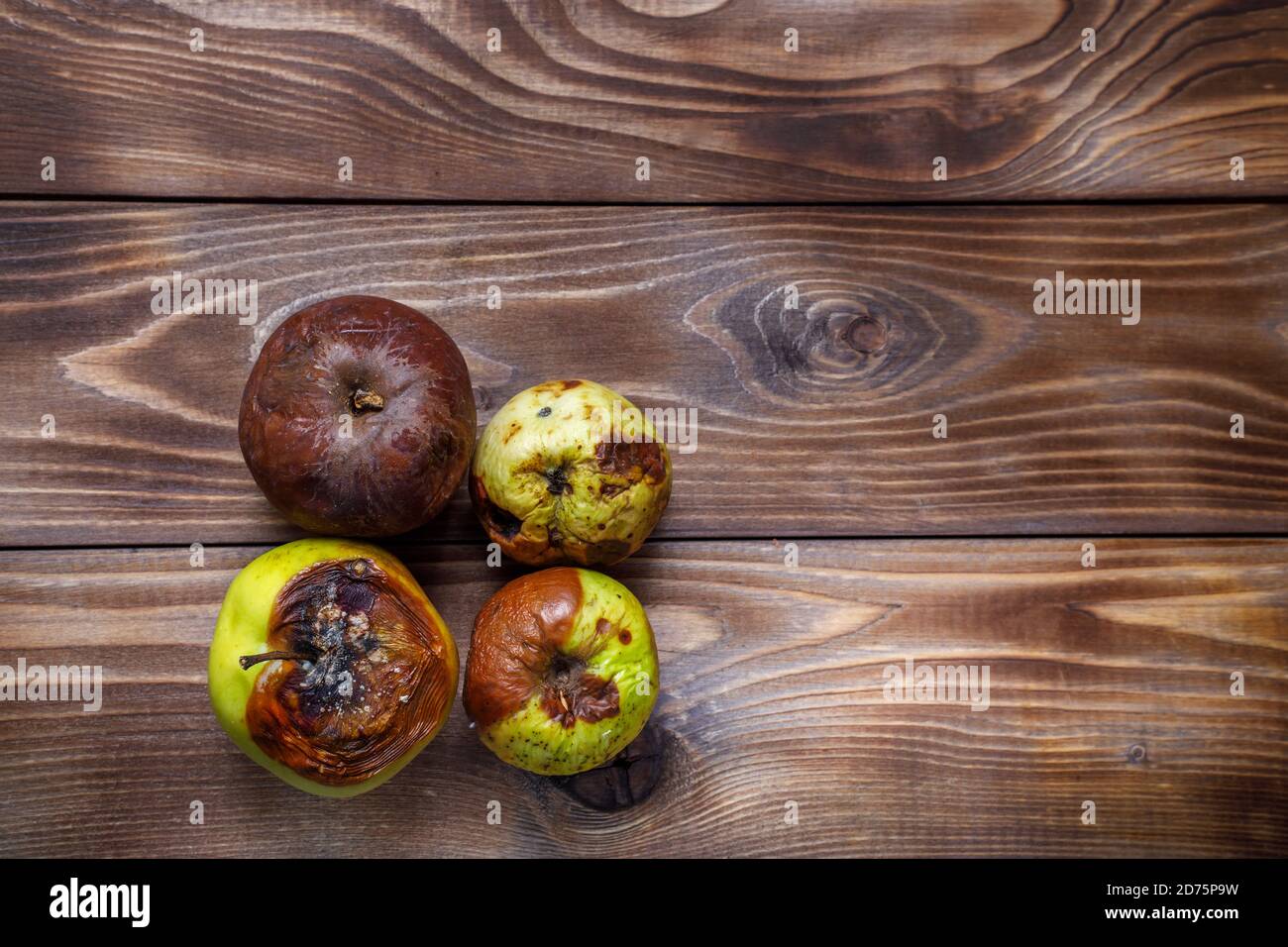 Rotten and moldy apples on a wooden background. Flat layout. Copy space Stock Photo