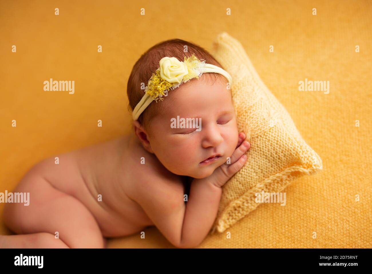 portrait of a beautiful seven day old baby girl. She is sleeping in a curled up fetal position on a yellow blanket Stock Photo