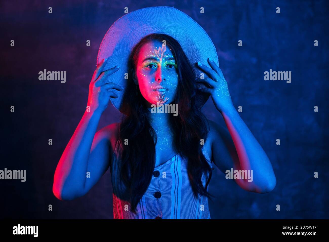 Portrait of beautiful woman in hat with fluorescent makeup on face and skin in ultraviolet light. Ethnic, esoteric and art concept. Stock Photo