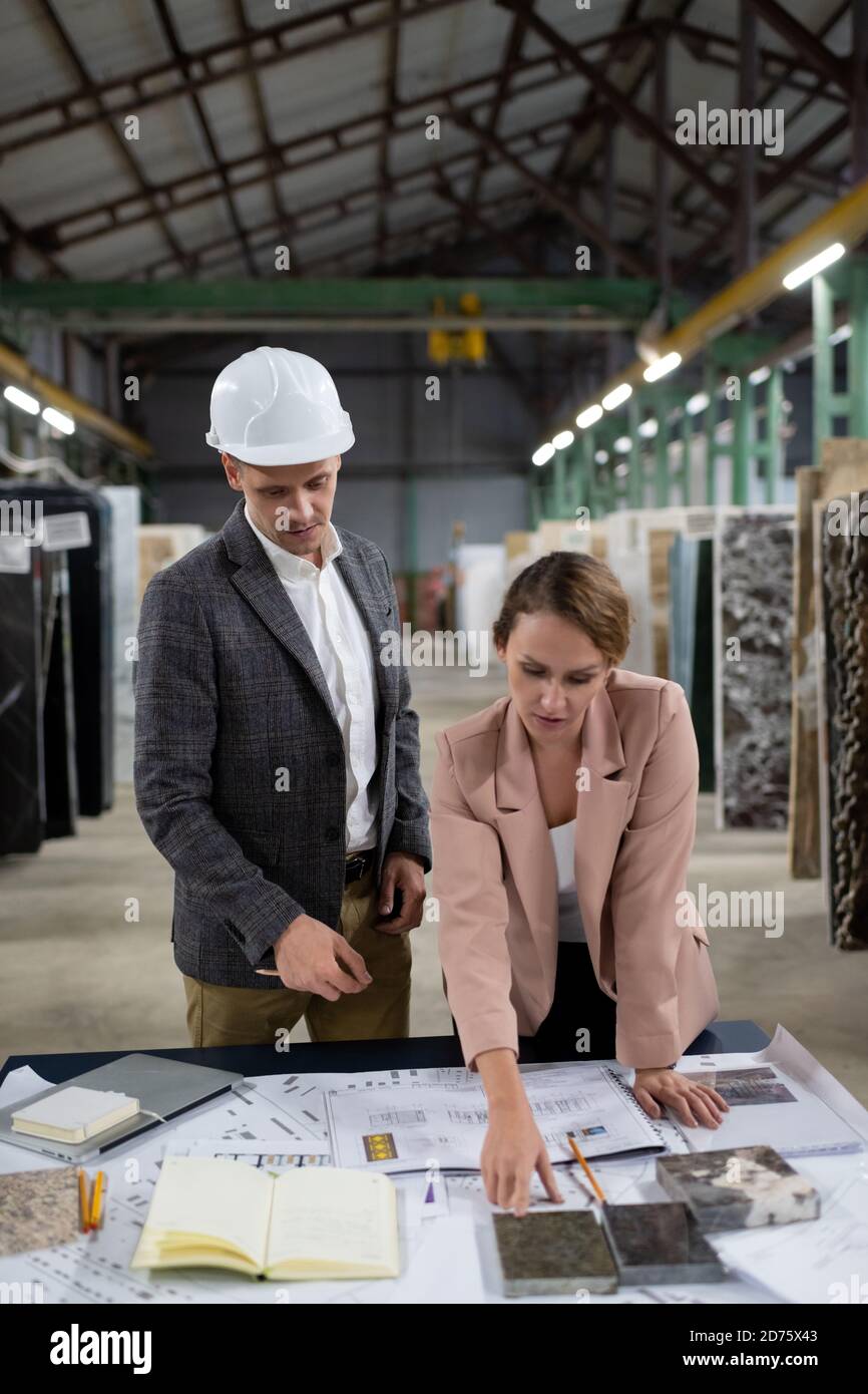 Elegant adult man and woman at table with blueprint and marble samples working on new project in storehouse Stock Photo