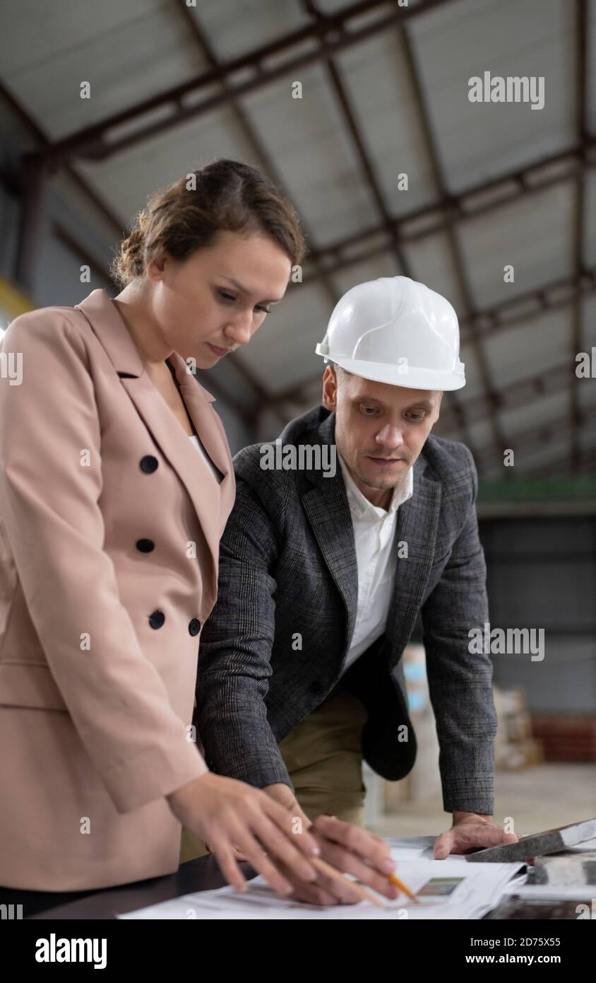 Low angle of man in hardhat and woman in jacket creating new architectural project examining draft in storage of stone company Stock Photo